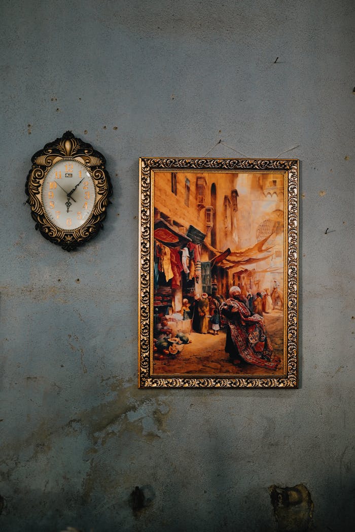 A classic wall decor with an ornate clock and framed painting on an aged wall.
