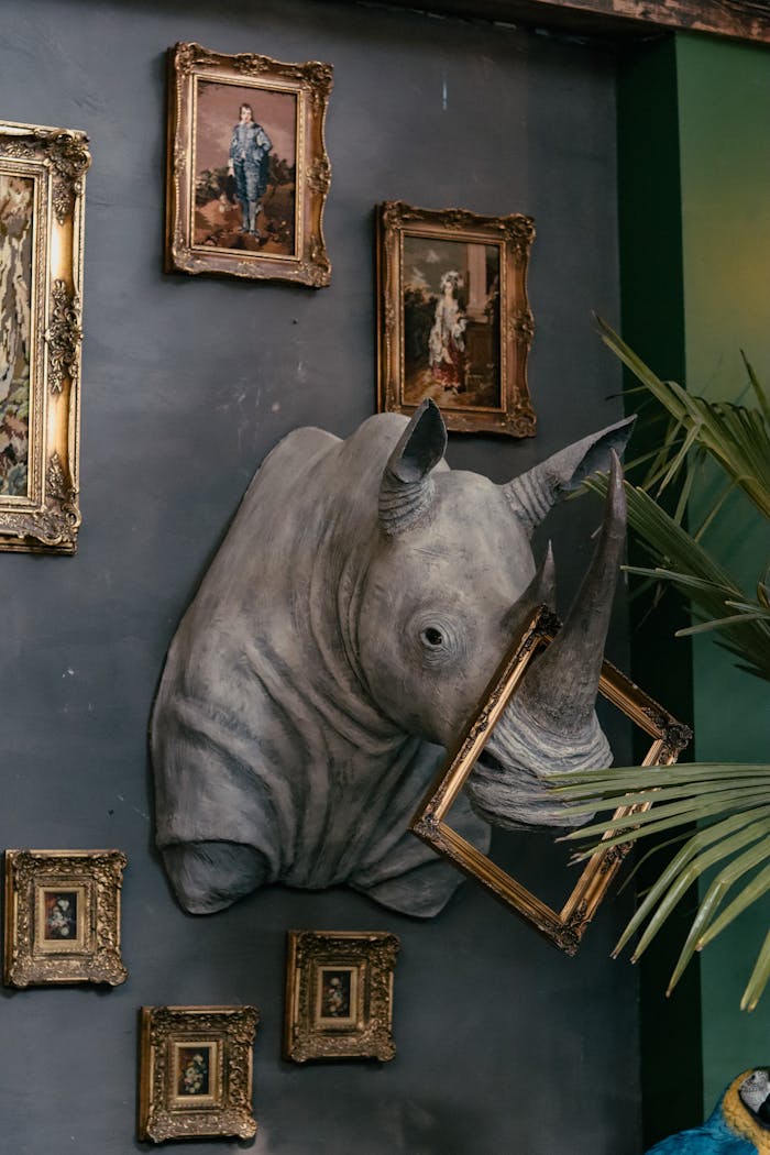 Unique home decor featuring a rhino sculpture and ornate framed paintings on a dark wall.